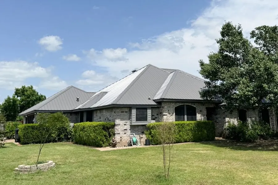 Brick home with metal roof surrounded by landscaping