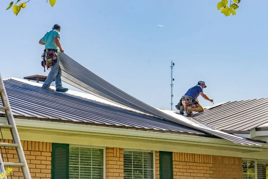 Two workers positioning metal panels on a roof